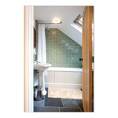 an attic bathroom with green tile and white fixtures, along with a skylight above the bathtub