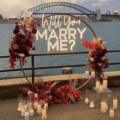 a sign that says will you marry me? surrounded by candles and flowers