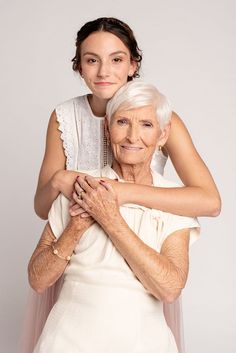 an older woman is hugging her younger lady's shoulders while she wears a white dress