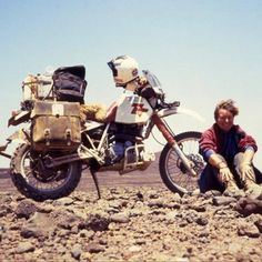 a man sitting on the ground next to a motorcycle with bags on it's back