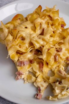 a white plate topped with macaroni and cheese next to a fork on a table