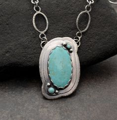 Beautiful Kingman Turquoise Stone with Handmade, One-of-a-Kind Sterling Silver Chain.  Oh, the color of this stone  Tons of time and love went into this piece featuring a lovely, large Kingman turquoise stone set in a scalloped, layered setting, with the added detail of Carico Lake turquoise and silver ball embellishments. I added even more love by texturing the edges of the layered setting and making every link of the matching, textured, handmade chain.  Truly unique and definitely one-of-a-kind.  Details: ~    Pendant measures 1 5/8" long & slightly more than 1" wide ~   The large stone is from the Kingman, AZ mines and has been cut & stabilized by an AZ lapidarist/jeweler. ~    Two small stones are Carico Lake from Lander County, Nevada and have been cut by an American lapidarist. ~ Artisan Turquoise Necklace With Large Stone, Unique Turquoise Necklace With Large Stone, One Of A Kind Oval Turquoise Necklace, Artisan Turquoise Oval Necklace, Handmade Artisan Turquoise Oval Necklace, Handmade Artisan Oval Turquoise Necklace, Artisan Handmade Oval Turquoise Necklace, Turquoise Jewelry With Large Round Stone Pendant, Turquoise Round Pendant With Large Stone