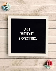 a black and white framed sign with the words act without expecting on it next to flowers