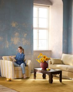 a woman sitting on a chair in a room with blue walls and sunflowers