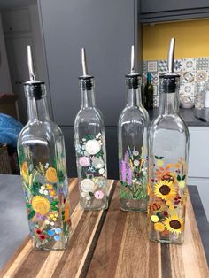 three glass bottles with flowers painted on them sitting on a wooden table in a kitchen