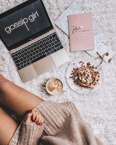 a woman sitting on the floor next to her laptop and coffee cup, with some food in front of her