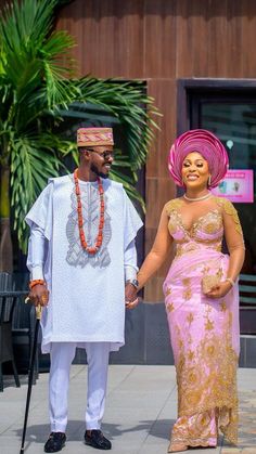 a man and woman dressed in traditional african garb holding hands while walking down the street