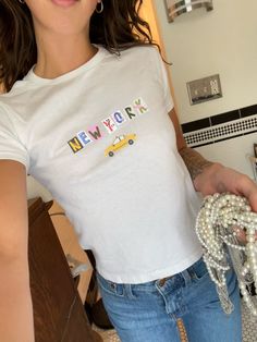 Looking for the perfect y2k baby tee for yourself or as a gift? This cute New York baby tee shirt makes the perfect gift for her. Pick up this cute aesthetic baby tee today to bring back the nostalgic 90s/y2k style! ✅ SHIRT FEATURES -Authentic 90s/y2k Baby Tee Fit -Super Soft Feel -Crisp Graphic Print -Eco-Friendly Process 📦 PROCESSING & SHIPPING All apparel ships within 1-3 days and takes another 1-4 days in transit. Your custom order will be there before you know it! 📏 SHIRT SIZING (also see Graphic Baby Tee Outfit, Baby Tee Designs, Y2k Style Short Sleeve T-shirt With Logo Print, Y2k Style Short Sleeve T-shirt With Slogan, Y2k Style Short Sleeve T-shirt With Text Print, Oddli Custom Baby Tee, Y2k Style Slogan T-shirt With Short Sleeves, Graphic Baby Tees Aesthetic, 90s Inspired Short Sleeve T-shirt With Text Print