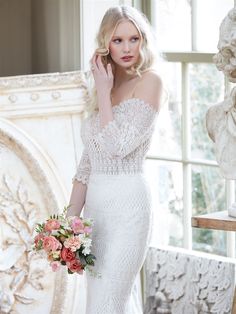 a woman in a white wedding dress holding a bouquet and posing for the camera with her hand on her face