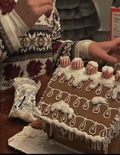 a person decorating a gingerbread house with white icing and candy canes