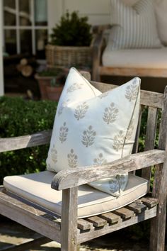 a wooden chair with a pillow on it sitting in front of a couch and some bushes