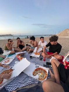 a group of people sitting on top of a beach next to each other eating pizza