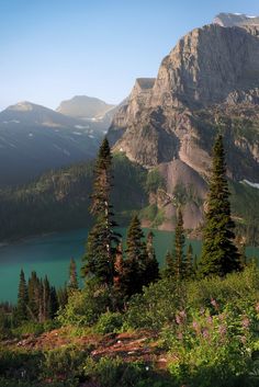 the mountains are covered in snow and green trees near a lake with blue water surrounded by evergreens