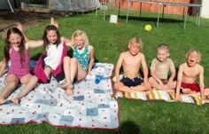 a group of kids sitting on top of a blanket in the grass next to each other