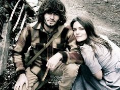 a man and woman sitting next to each other on the ground in front of a fence