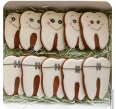 decorated cookies in the shape of teeth are arranged in an open box with grass inside