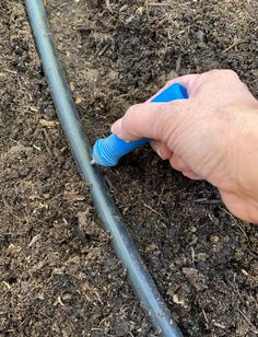 a hand is holding a blue hose in the dirt