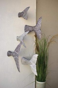 three metal birds hanging on the side of a wall next to a potted plant