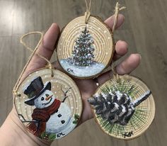 hand holding three christmas ornaments in front of a wood flooring background with a tree and snowman