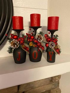 three red candles sitting on top of a mantle with christmas decorations and pine cones in them