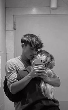 a man and woman hugging in front of a mirror while looking at their cell phone