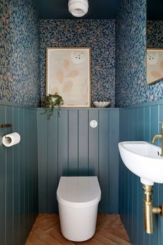 a white toilet sitting next to a sink in a bathroom under a painting on the wall