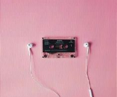 an old fashioned cassette player with ear buds plugged into the cord, on a pink striped background