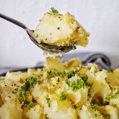 a spoon full of potatoes with parsley sprinkled on it and being lifted from the casserole