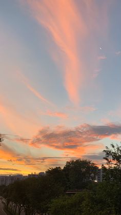 the sky is pink and orange as the sun sets in the distance behind some trees