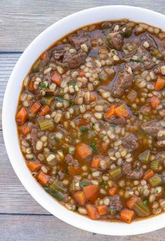 beef barley soup in a white bowl with carrots and celery on the side