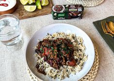 a white plate topped with rice and meat next to a glass of water on top of a table