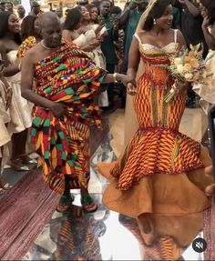 two women dressed in african clothing walking down the aisle with other people behind them and holding hands