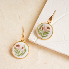 a pair of earrings with flowers on them sitting on top of a white napkin next to a gold fork