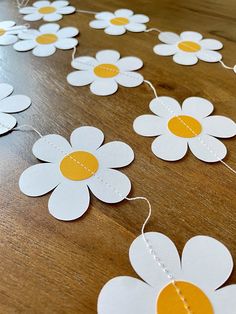 white and yellow paper daisies are strung on a wooden table with string for decoration