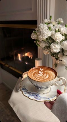 a cup of coffee sitting on top of a saucer next to a vase with flowers