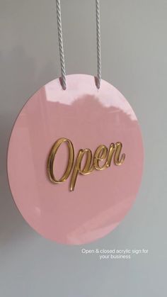 a pink round sign with the word open hanging from it's sides and two silver strings