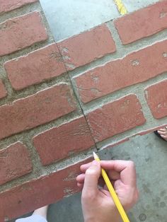 a person holding a pencil in front of a brick wall