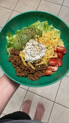 a green plate topped with lots of food on top of a tiled floor next to someone's feet