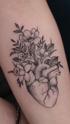 a heart tattoo with flowers and leaves on the side of the arm, it is black and white