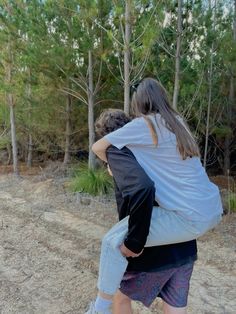 two people are walking in the woods with their backs to each other and one is carrying another person on his back