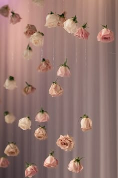 pink and white flowers hanging from strings in front of a purple wall with light colored curtains