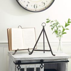 an open book sitting on top of a wooden table next to a clock and potted plant