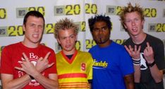 four young men posing for the camera in front of a wall