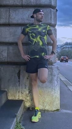 a man leaning against a stone wall with his hands on his hips wearing running shorts