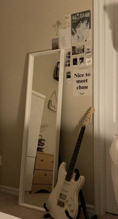 an electric guitar sitting in front of a mirror next to a dresser and door with pictures on it