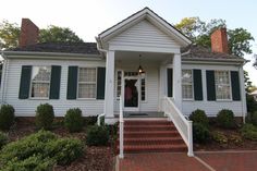 a white house with green shutters and steps leading to the front door is shown