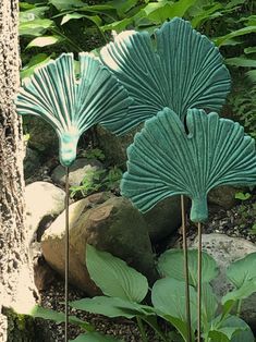 two green leaf sculptures sitting next to each other on top of a pile of rocks