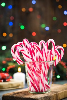 some candy canes are in a glass on a wooden board with christmas lights behind them