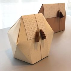 two origami boxes with tassels on them are sitting on a table