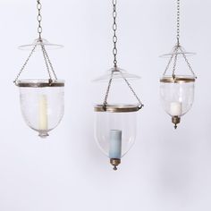 three hanging glass lanterns with chains and candle holders on each one, all suspended from the same ceiling